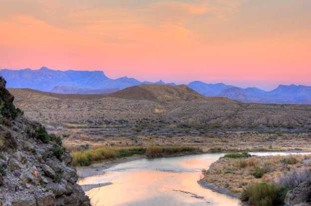 Image shows the river flowing into the mountains around a bend at sunset in Big Bend National Park, Texas.