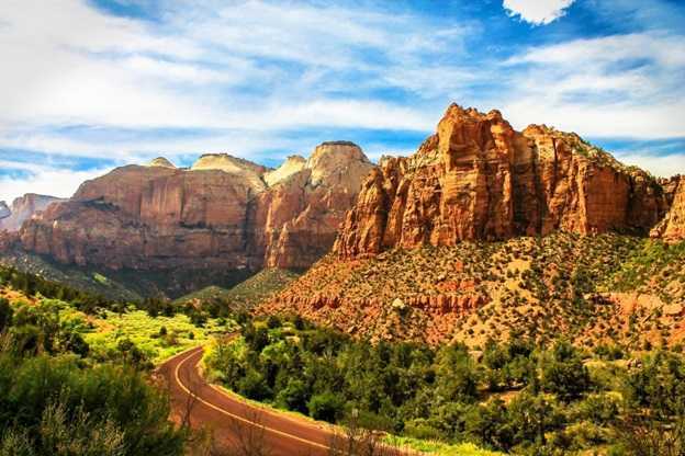 Image shows a two-lane roadway winding through the mountains in Zion National Park, Utah