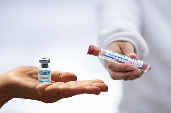 holding a sample test bottle of covid 19 vaccine with blood test tube