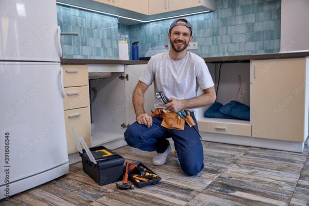 male plumber sitting next to open kitchen drawer with toolkit