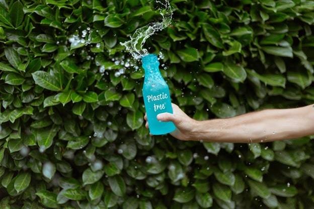 a person sprinkling water in a blue bottle with a plastic-free print in front of green bay laurels