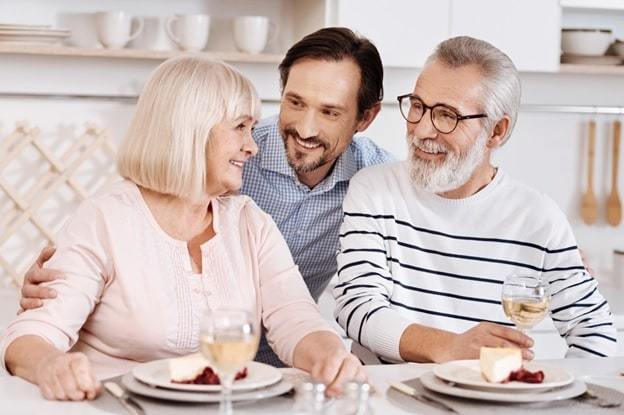 cheerful mature son hugging elderly parents at home