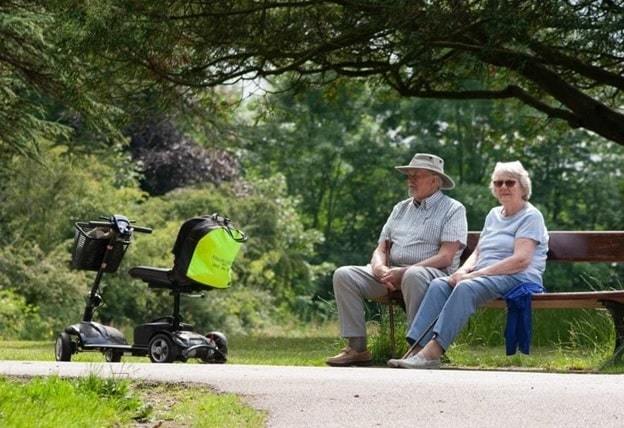 senior citizen sitting on bench with mobility scooter