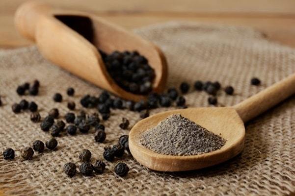 ground black pepper and peppercorns with wooden spoon and scoop