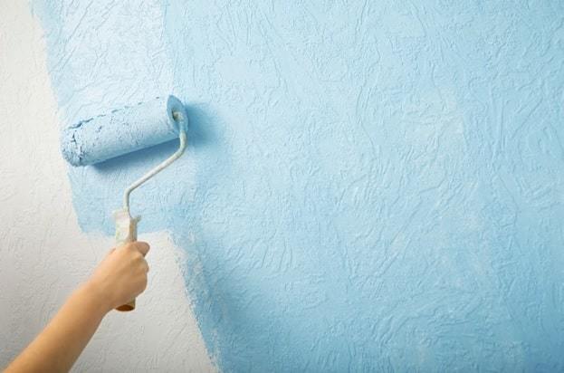 holding blue color rolling brush painting the white wall