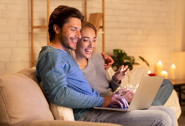 beautiful couple looking at laptop smiling sitting on sofa