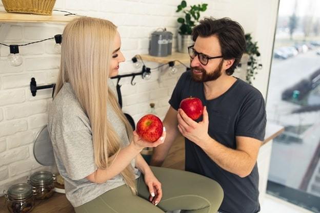 cute couple sitting in their modern kitchen holding apple