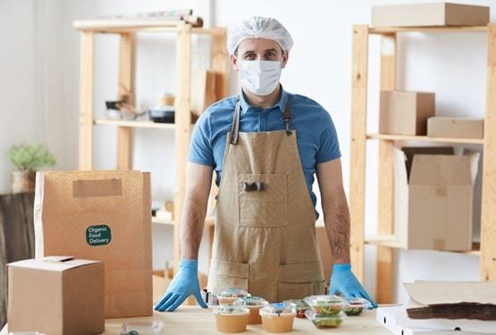 man wearing protective gloves and apron safely packaging orders