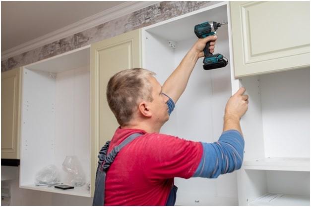 handyman fixing the kitchen cabinet doors with battery drill