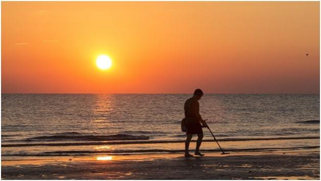 man on beach with metal detector at sunset