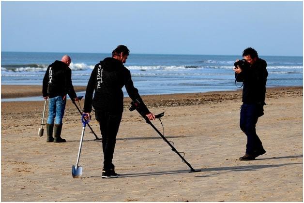 men with metal detectors and photographer on beach