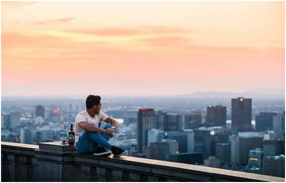 a person sitting on the roof of a tall building and enjoying the sunset with a view of the city