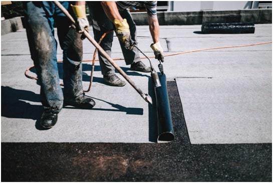 construction workers insulating rooftop with bituminous membrane