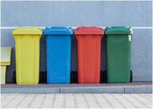 four assorted-color trash bins beside gray wall