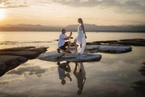 man proposing with engagement ring by lake at sunset with mountains