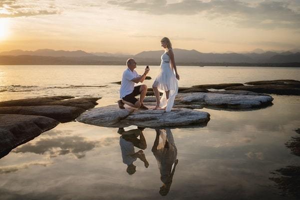 man proposing with engagement ring by lake at sunset with mountains