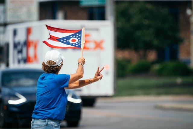 person waving the Ohio flag and holding out the peace sign, moving, a transport truck