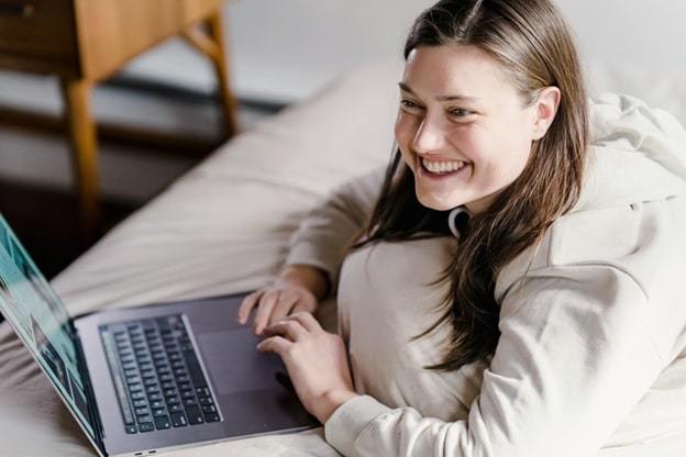 cheerful woman working on laptop in bedroom