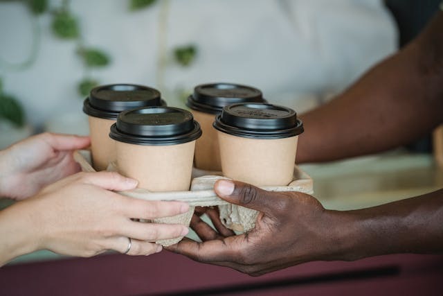 person handing a drink carrier with four coffee cups