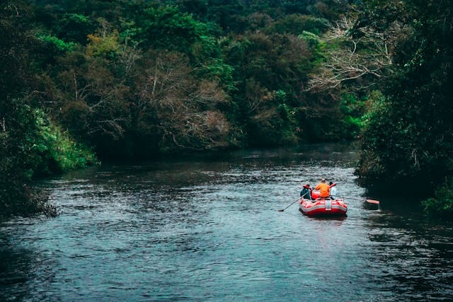 three persons riding red inflatable raft