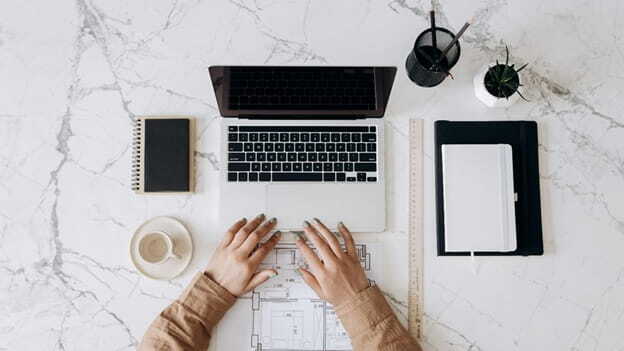 person in brown long sleeve shirt using macbook pro beside white ceramic mug