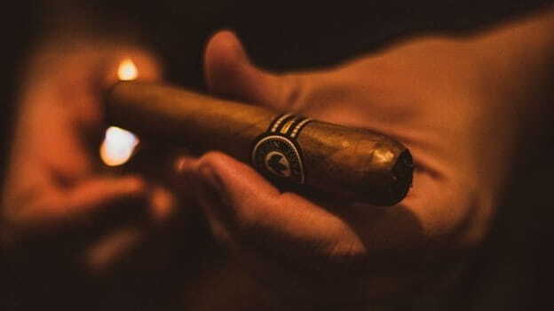 a detailed close-up shot of a hand lighting a cigar in a dark setting