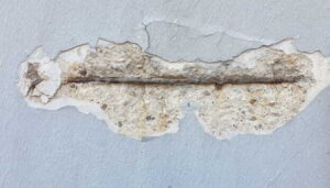 damaged concrete wall with peeling paint and exposed metal bar