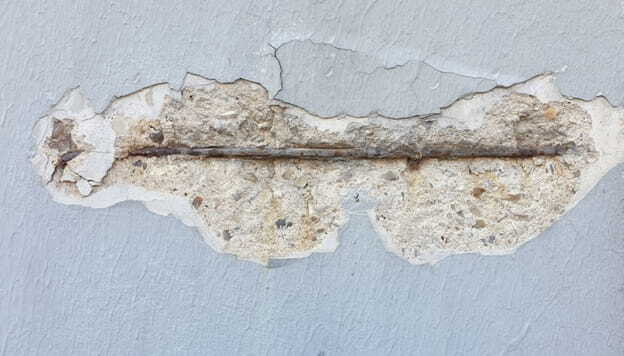 damaged concrete wall with peeling paint and exposed metal bar